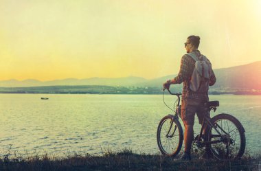 Sahil bisiklet ile ayakta ve manzarayı günbatımı tatil kavramı dinlenme hedef seyahat bisikletçi genç adam