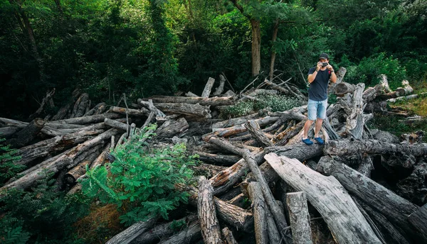 Joven viajero hombre se para en los registros y toma fotos en la cámara del teléfono inteligente con el espacio de copia izquierda — Foto de Stock