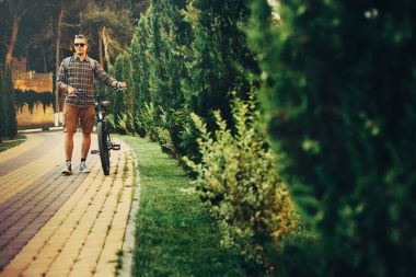 Genç adam Bisikletin üstünde yaz Park tatil hafta sonu etkinliği ile yürüme güneş gözlüğü