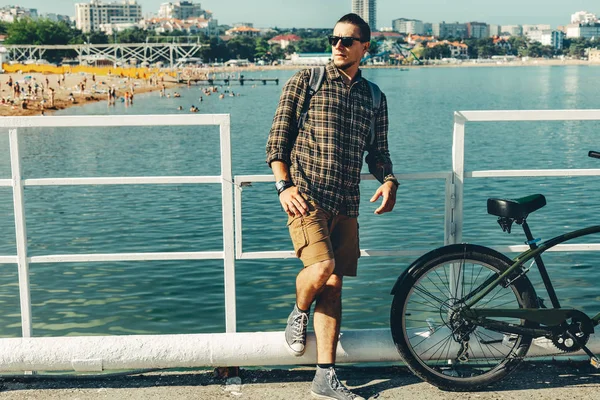 Joven ciclista se para en el muelle y disfruta de la vista al mar. Concepto de actividad de viajes de vacaciones — Foto de Stock
