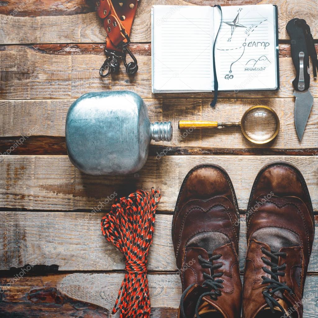 Hiking accessories on wooden background: old hiking leather boots, vintage film camera, travel notebook, knife. Lifestyle concept adventure vacations outdoor. Flat lay style