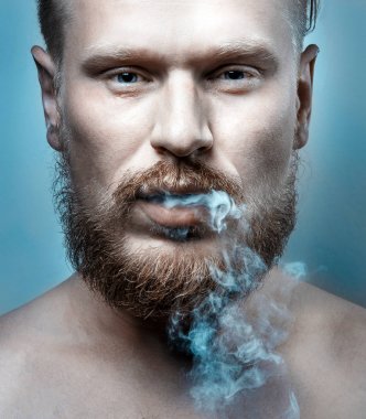 Portrait Of A Handsome Man With A Beard, Cigarette Smoke Coming Out Of His Mouth, Close-up. Harmful Habit Concept clipart