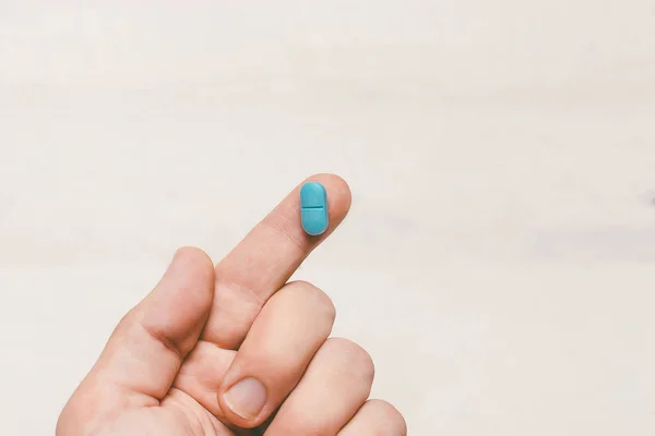 Jeden prst držící modrou pilulku na bílém pozadí dřevěná — Stock fotografie