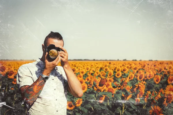 Porträtt av manlig fotograf att foto med kameran i händerna utomhus på solrosor fält med tonade Filter — Stockfoto