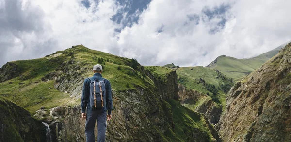 Homem caminhante com mochila e Pólos de Trekking descansando e olhando para as montanhas no verão ao ar livre, vista traseira — Fotografia de Stock