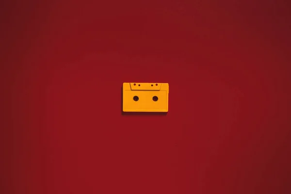 Cassete de áudio amarelo no centro fitas no fundo vermelho, vista superior. Conceito criativo de tecnologia retro — Fotografia de Stock