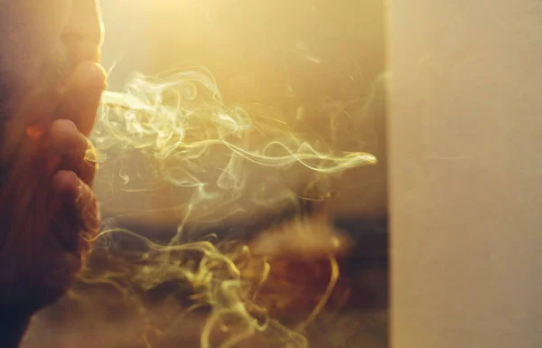Hombre irreconocible sostiene un cigarrillo en la mano y fuma contra el telón de fondo de un sol brillante. Concepto de retrato de creatividad —  Fotos de Stock