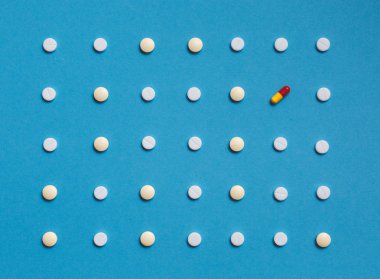 Pattern with white tablets and one Colored Pill On Blue Background. Medicine Healthcare Pharmacy Concept clipart
