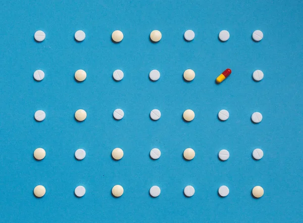 Modèle avec des comprimés blancs et une pilule de couleur sur fond bleu. Médecine Soins de santé Pharmacie Concept — Photo