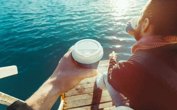 Two men drinking coffee sitting on the pier and enjoying the sea view, Point Of View Shot