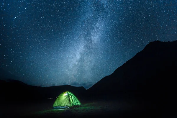 A tent glows under a night sky Milky May full of stars. Elbrus National Park, Russia