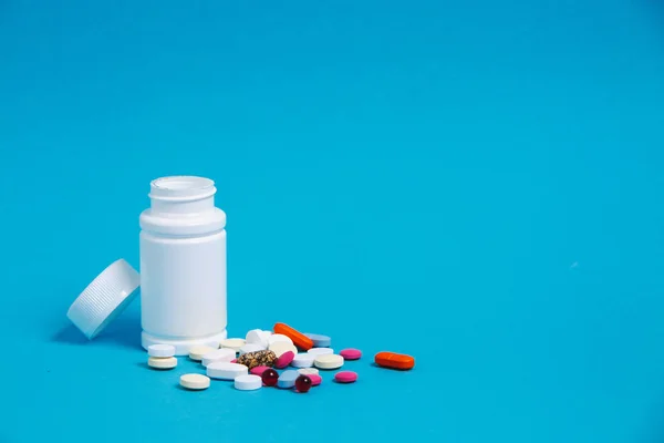 Sokszínű tabletták és fehér üveg, a kék háttér, elülső kilátás. Gyógyszer gyógyszertár egészségügyi koncepció — Stock Fotó