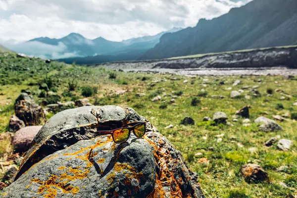 Hiking Vacation Tourism Concept. Sunglasses lie on a stone in the background of a mountain landscape — Stock Photo, Image