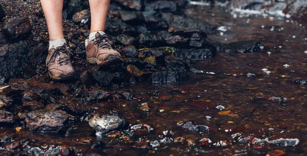 Patas femeninas en botas de trekking. Una viajera cruza el río. Aventura, turismo y concepto de estilo de vida — Foto de Stock