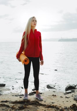 Pratik yaptıktan sonra yoga minderi olan çekici bir kız. Deniz kenarındaki Biyohack Spor Sağlığı