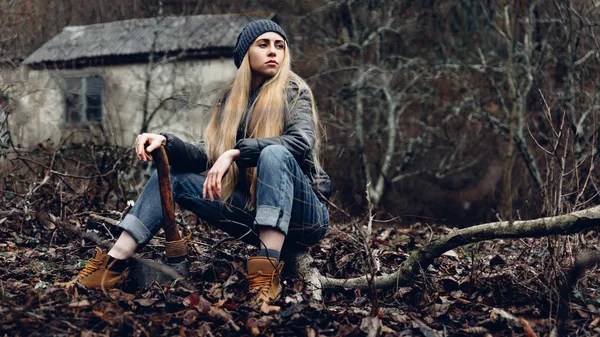Atractiva chica descansando en el bosque sostiene un hacha en las manos. Concepto de supervivencia de bosquejos — Foto de Stock