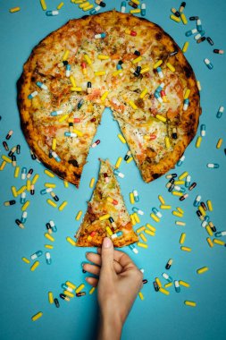 Female Hand Holds In Hand A Piece Of Pizza Sprinkled With Pills, Top view Idea. Biohacking Healthy Food Concept clipart