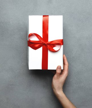 Kadın El Kırmızı Kurdeleye Sarılı Hediyesini Gri Arka plan Görünümünde Veriyor. Doğum günü, Sevgililer Günü, Yıldönümü, Tatil Konsepti