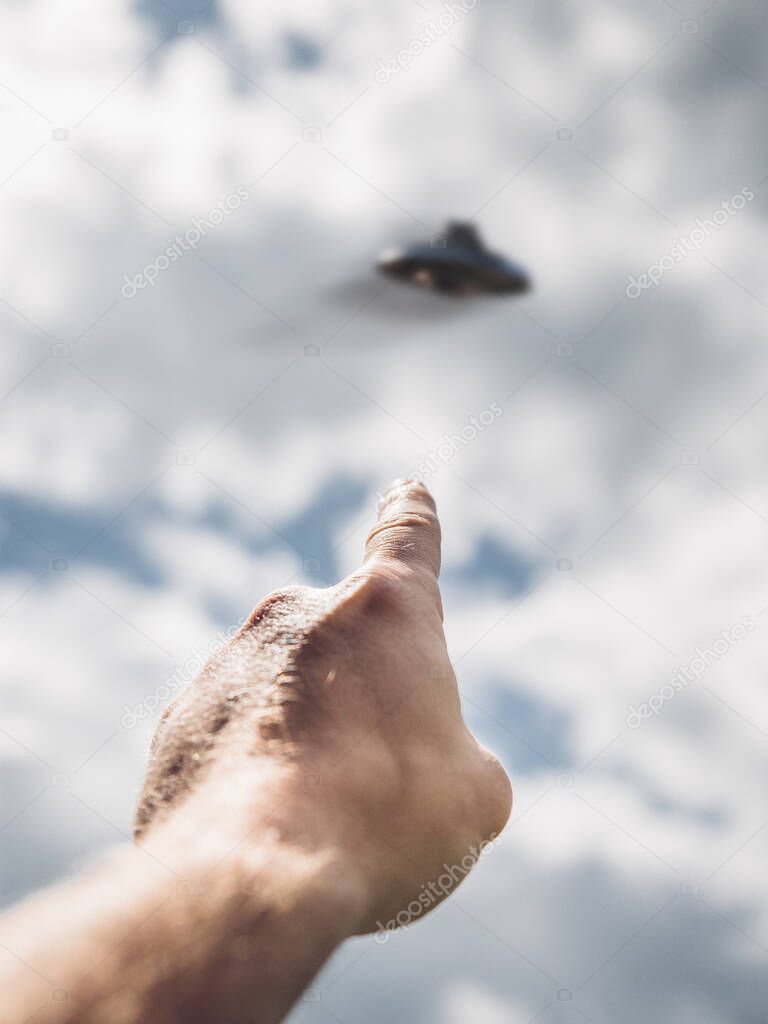 Male hand points to Unidentified flying object in sky, point of view. UFO Day Concept