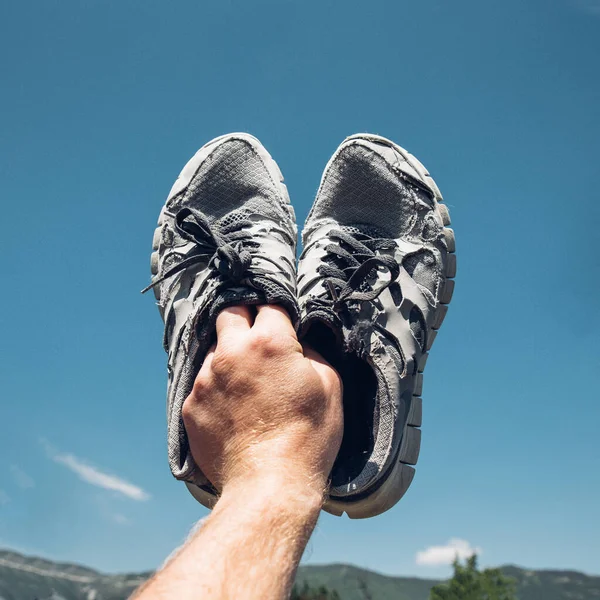 Hombre Sostiene Viejo Corriendo Zapatillas Mano Fondo Cielo Azul Montañas — Foto de Stock