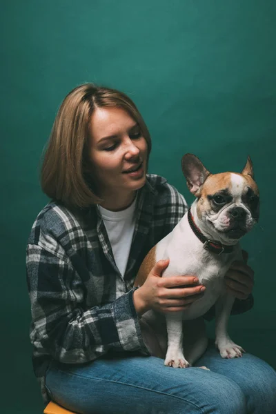 young girl and hugs a french bulldog on a green background