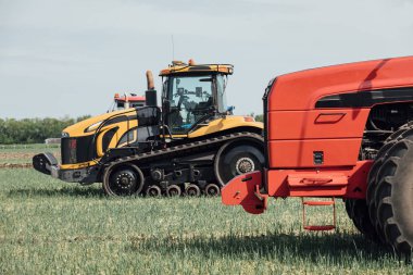 Sarı tırtıl ve kırmızı traktör mavi gökyüzüne karşı tarlada büyük tekerleklerle
