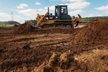 İnşaat alanında büyük sarı bir buldozer güneşli bir günde bir bina inşaatı için bir alan hazırlıyor.