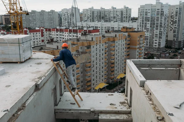 a builder on the top floor of a building under construction stands on a staircase in the middle of high-rise buildings in a densely populated residential area
