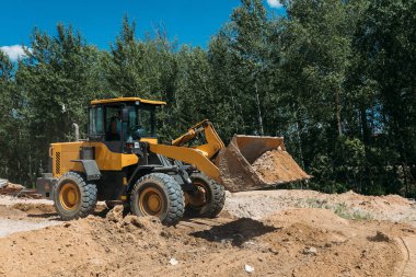 Büyük sarı traktör buldozerleri iş yerindeki kumda bir inşaat alanında.