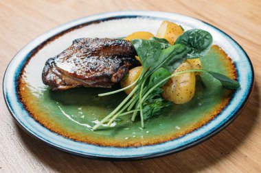 Kızarmış ördek, akşam yemeği için yeşil bir tabakta patates ve otla servis ediliyor.