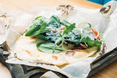 Etli, sebzeli, soslu ve otlu taze pide bir tortilla ve bir restoranda ahşap tepside servis edilir.