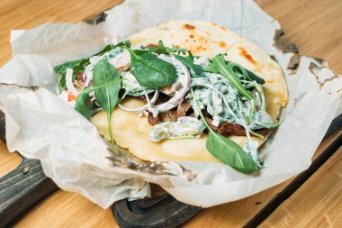 Etli, sebzeli, soslu ve otlu taze pide bir tortilla ve bir restoranda ahşap tepside servis edilir.