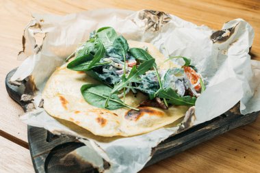 Etli, sebzeli, soslu ve otlu taze pide bir tortilla ve bir restoranda ahşap tepside servis edilir.