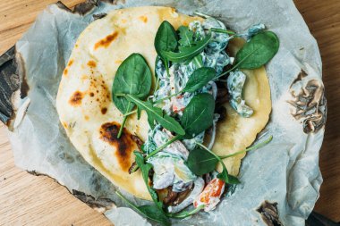 Etli, sebzeli, soslu ve otlu taze pide bir tortilla ve bir restoranda ahşap tepside servis edilir.