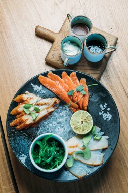 Limonlar, yosunlar ve soslarla dolu büyük bir tabakta çeşitli balık tabakları.