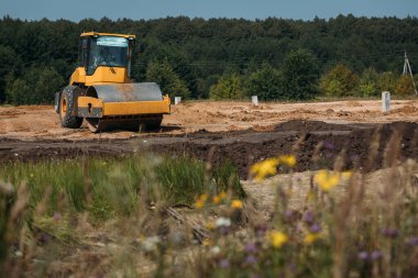 Sarı asfalt kaldırıcı sıkıştırıcısı güneşli bir günde bir inşaat alanında kumlar üzerinde çalışıyor.