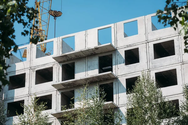 concrete blocks of an apartment building under construction on a sunny day through foliage