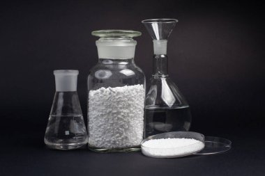 Siyah arka planda gevşek beyaz sentetik kauçuk örnekleri olan cam laboratuvar kavanozu.