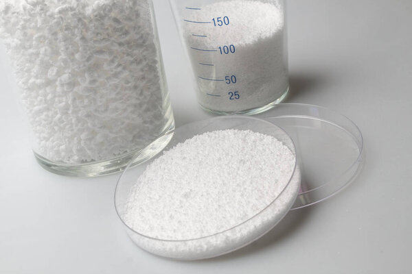 glass laboratory jar with samples of loose white synthetic rubber on a white background