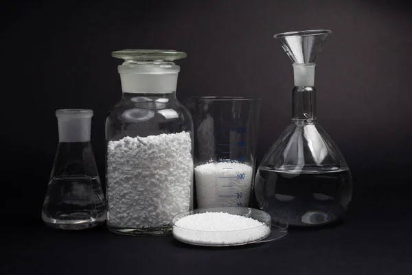 ガラス製の実験室用瓶に白い合成ゴムのサンプルと黒の背景に白いゴムのキューブ — ストック写真