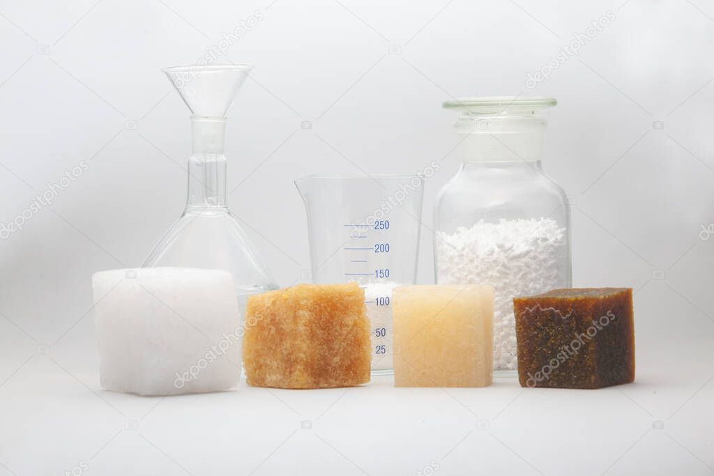 four multi-colored samples of a cube of polymer synthetic rubber and laboratory glass jars in the background shot on a white background