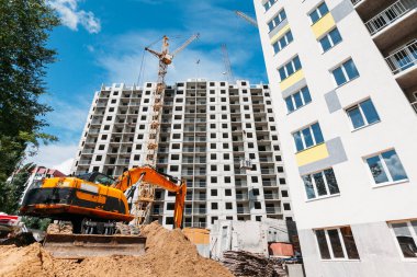 Turuncu kazıcı, inşaat halindeki bir inşaat sahasında ve çok katlı bir binada çalışıyor.