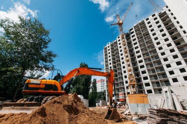 Turuncu kazıcı, inşaat halindeki bir inşaat sahasında ve çok katlı bir binada çalışıyor.