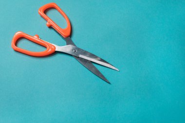 Mavi arka planda turuncu saplı metal makas düzgünce yerleştirilmiş.