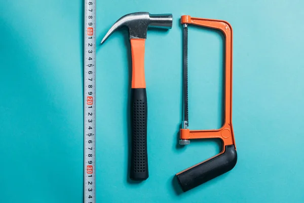 hammer, hacksaw, saw, tape measure with an orange handle on a blue background laid neatly