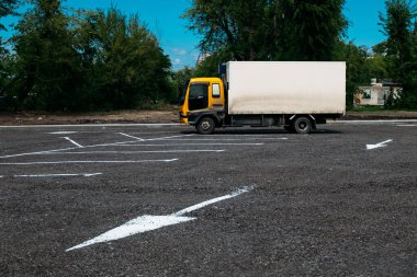 Küçük bir kamyon, sarı bir taksisi ve beyaz bir römorku olan otoparkta öğleden sonra yön okları olan.