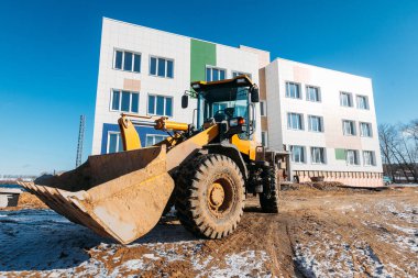 Baharda inşaat halindeki bir binanın arka planına yakın çekilen sarı buldozer kahvesi.