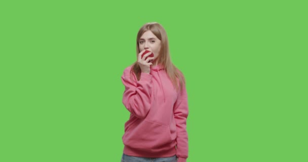Młoda kobieta je duże czerwone jabłko na tle klucza chroma — Wideo stockowe