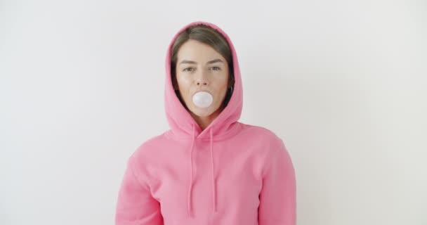 Κορίτσι ντυμένη με ροζ κουκούλα φυσάει τσιχλόφουσκα — Αρχείο Βίντεο