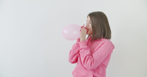 Νεαρή γυναίκα φυσάει ένα ροζ μπαλόνι — Αρχείο Βίντεο